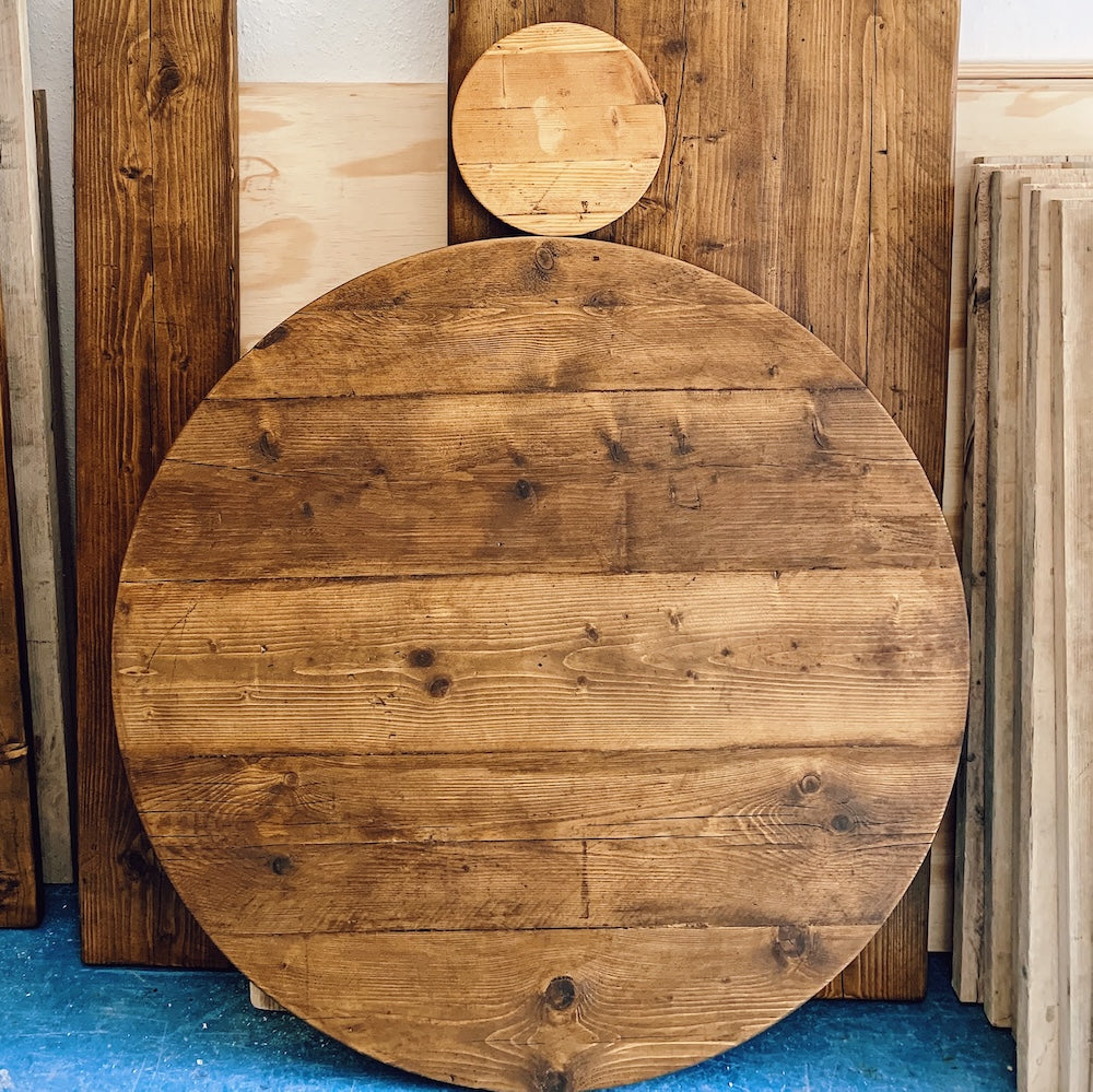 Handmade round solid wood tabletop leaning against timber boards in a woodworking workshop