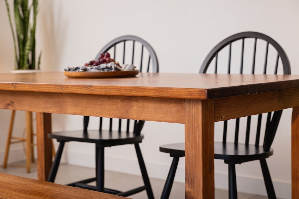 Solid wood dining table with handcrafted wooden legs and a smooth natural finish, shown with matching benches tucked underneath in a bright dining space.