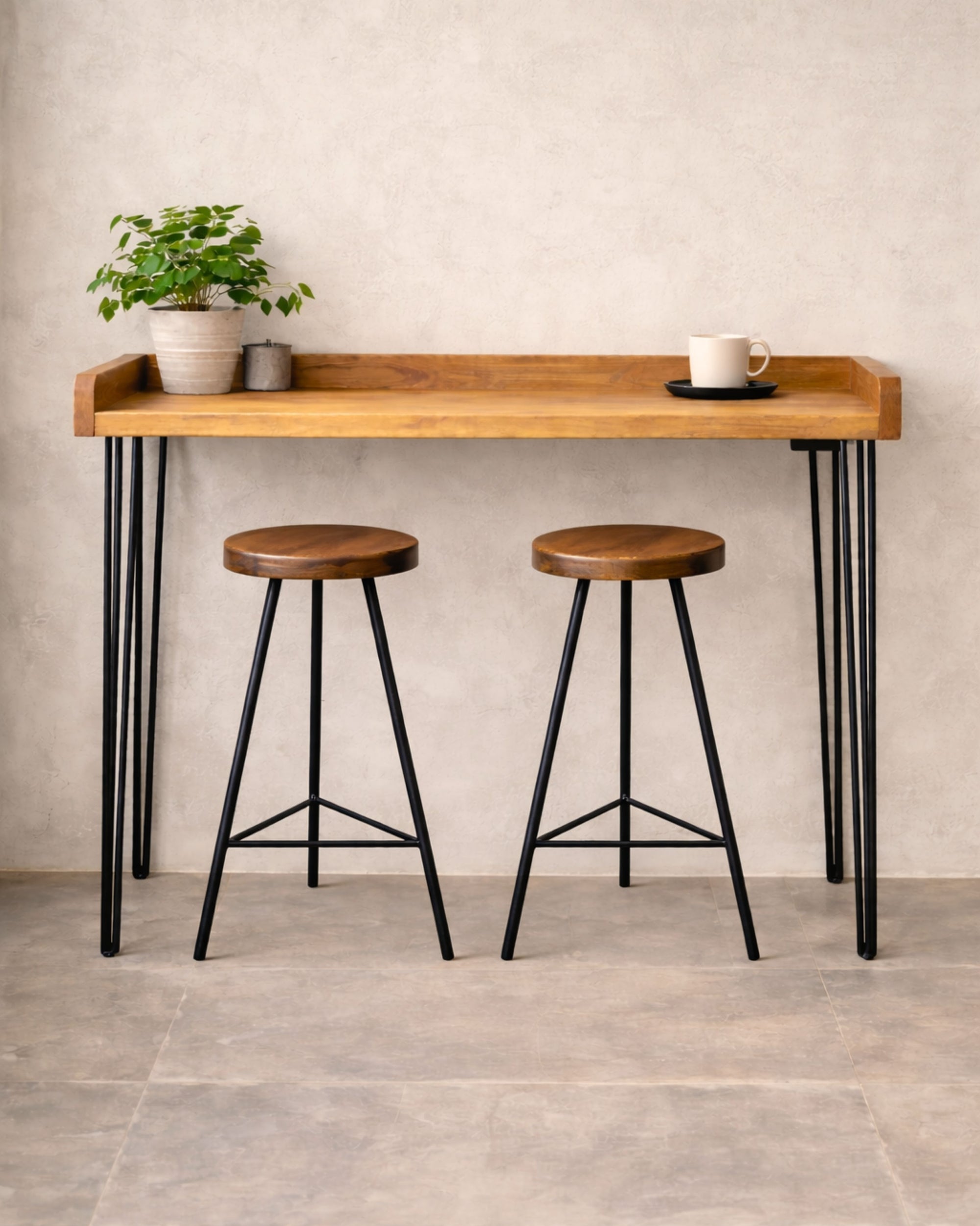 Handmade solid wood breakfast bar table with black hairpin legs and two stools beside a kitchen window, styled with a plant and coffee cup.