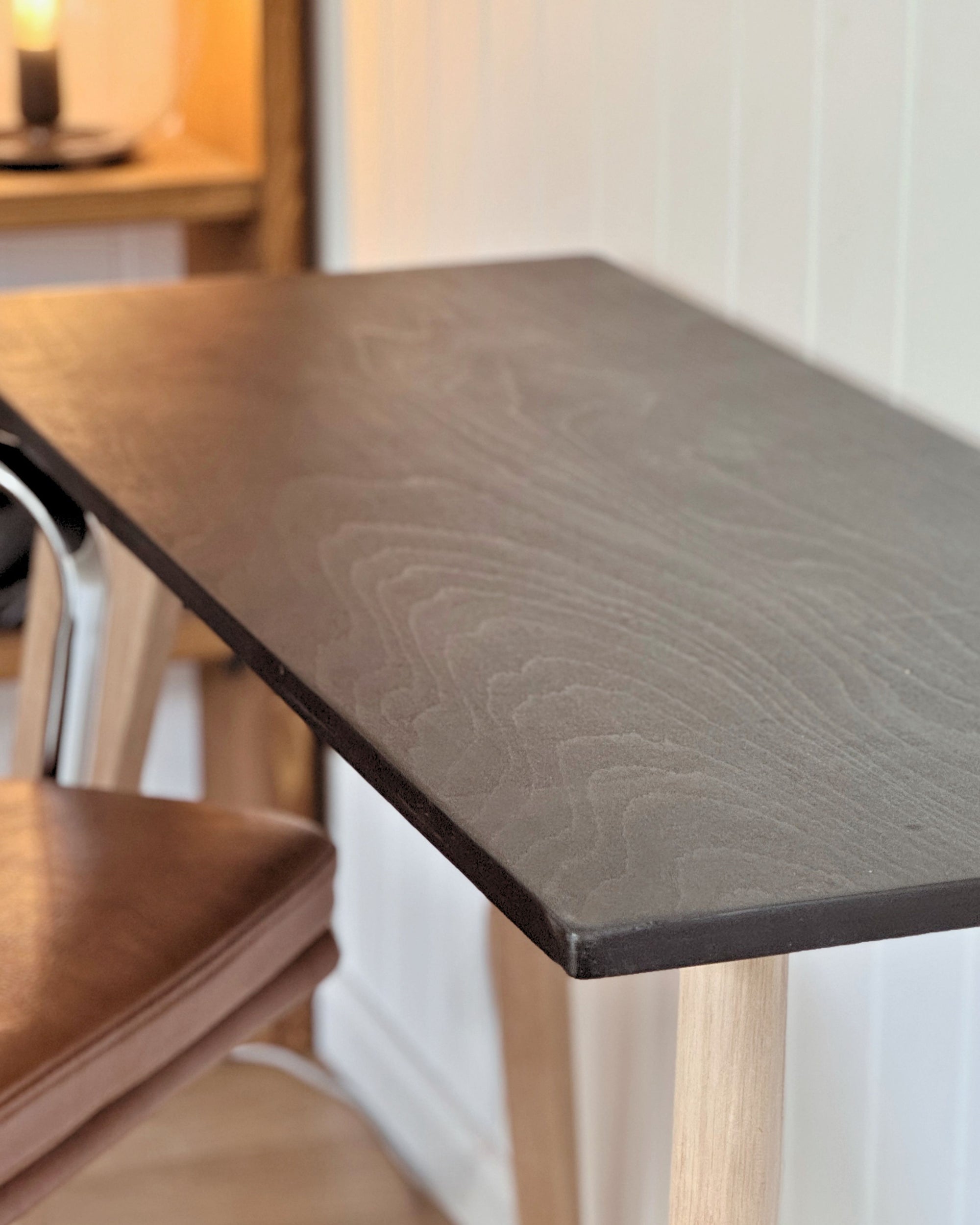 Scandi style minimalist desk with a black birch plywood top and natural light oak legs, set against a white panelled wall.